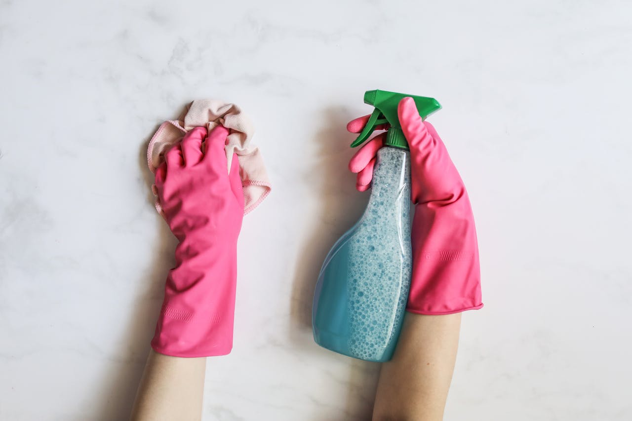 gallery-6 A pair of hands in pink gloves are cleaning with a spray bottle on a white background.